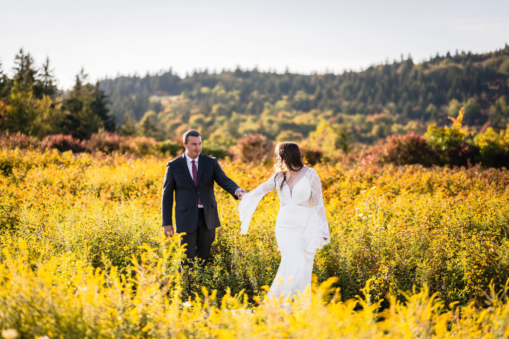 A marrier wearing a wedding dress leads her partner down a path in between wildflowers at Grayson Highlands State Park.