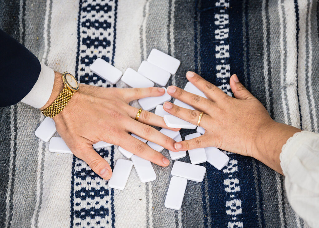 A close up photo of the wedding couple's hands shuffling a pile of dominos.