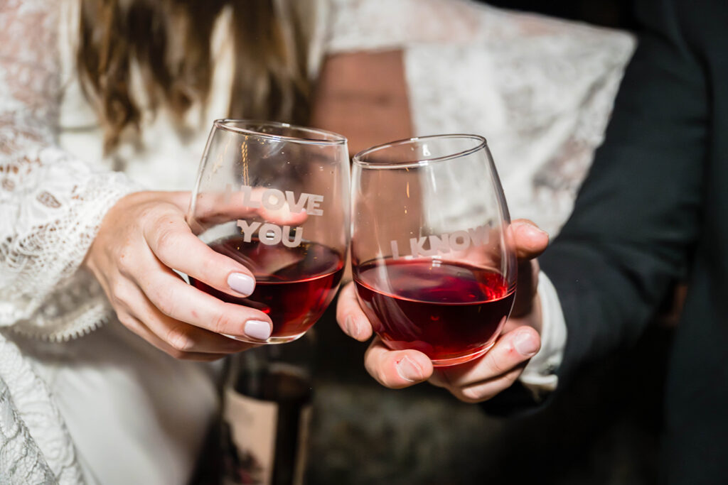 An elopement couple clinks their wine glasses on their wedding day. The inscription on the glasses read "I love you" and "I know", referencing Princess Leia and Han Solo's iconic lines from the Star Wars franchise.
