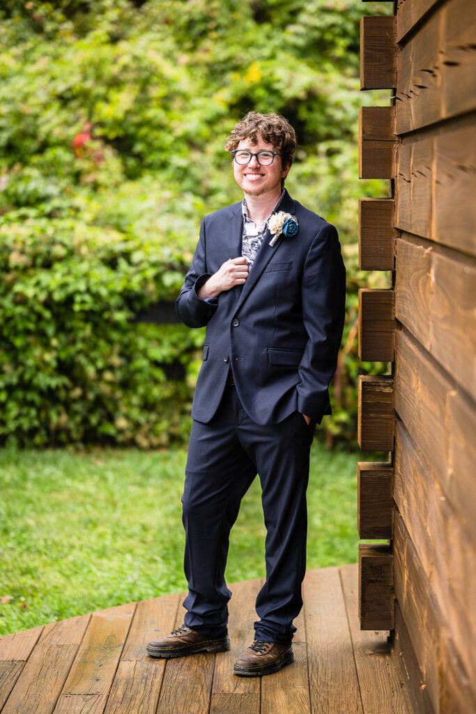 A queer marrier stands outside of a cabin for a portrait.