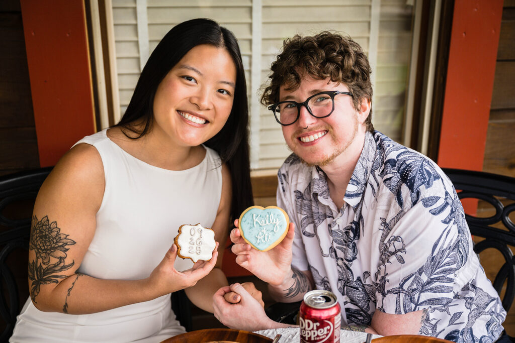 An elopement wedding couple sit on the porch of their Highland Hideaways cabin and smile together as they each hold a custom cookie.