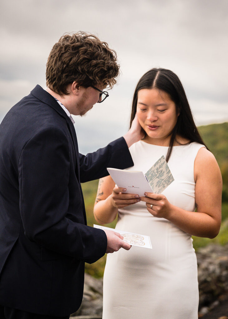 An LGBTQ+ marrier takes a deep breath in while reading a card. Their partner places their hand on her face to soothe her.