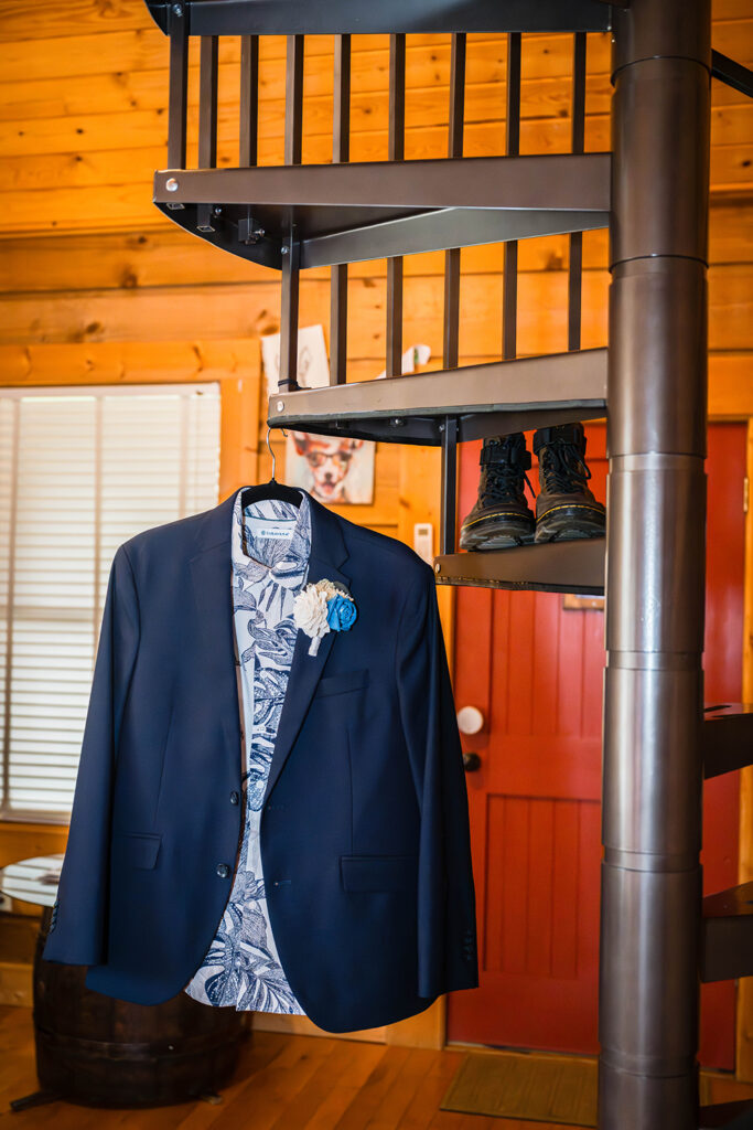 A navy blue suit jacket and a button down shirt with a monstera design is hung on a spiral staircase inside of a Highland Hideaways Airbnb. On one of the steps, there are a pair of Doc Marten boots.