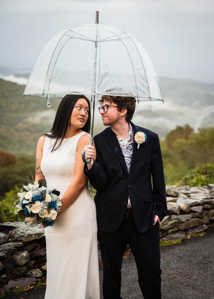 An LGBTQ+ couple strikes a dramatic pose under an umbrella on their rainy Grayson Highlands State Park elopement wedding day.