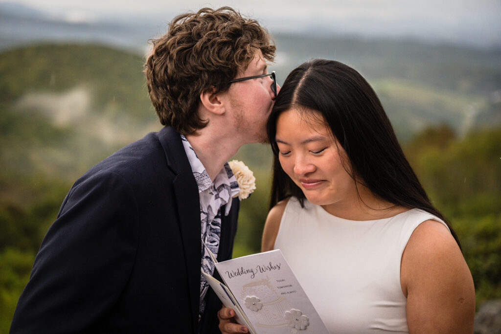 A queer marrier kisses the side of his partner's head as she starts to tear up while reading a card from a friend during their Grayson Highlands State Park wedding ceremony.