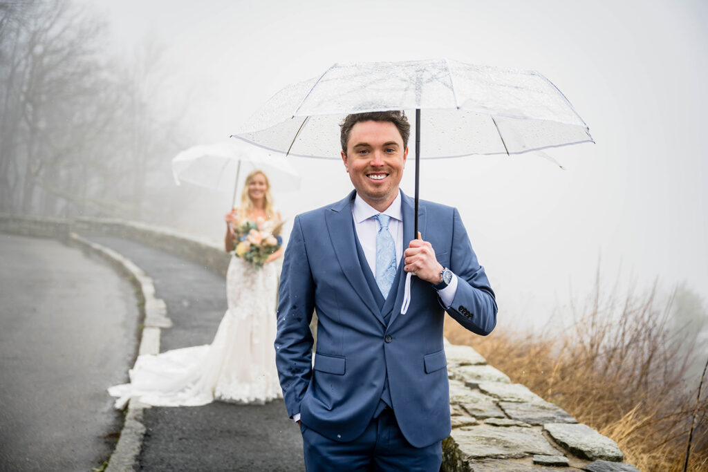 A groom smiles underneath an umbrella as he waits to see the bride for the first time in her wedding dress at Thorofare Mountain Overlook in Shenandoah National Park.